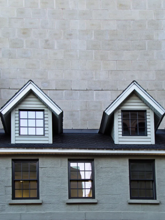 Twin dormer windows set into a dark shingle roof on a repainted house